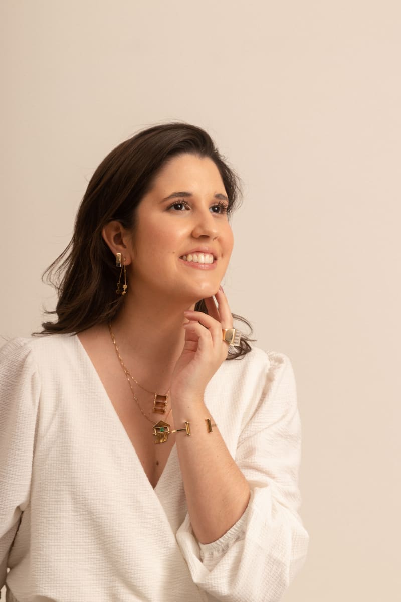 Tatiana Torres sorrindo, de blusa branca, usando colares, brincos e pulseira de ouro de sua própria criação